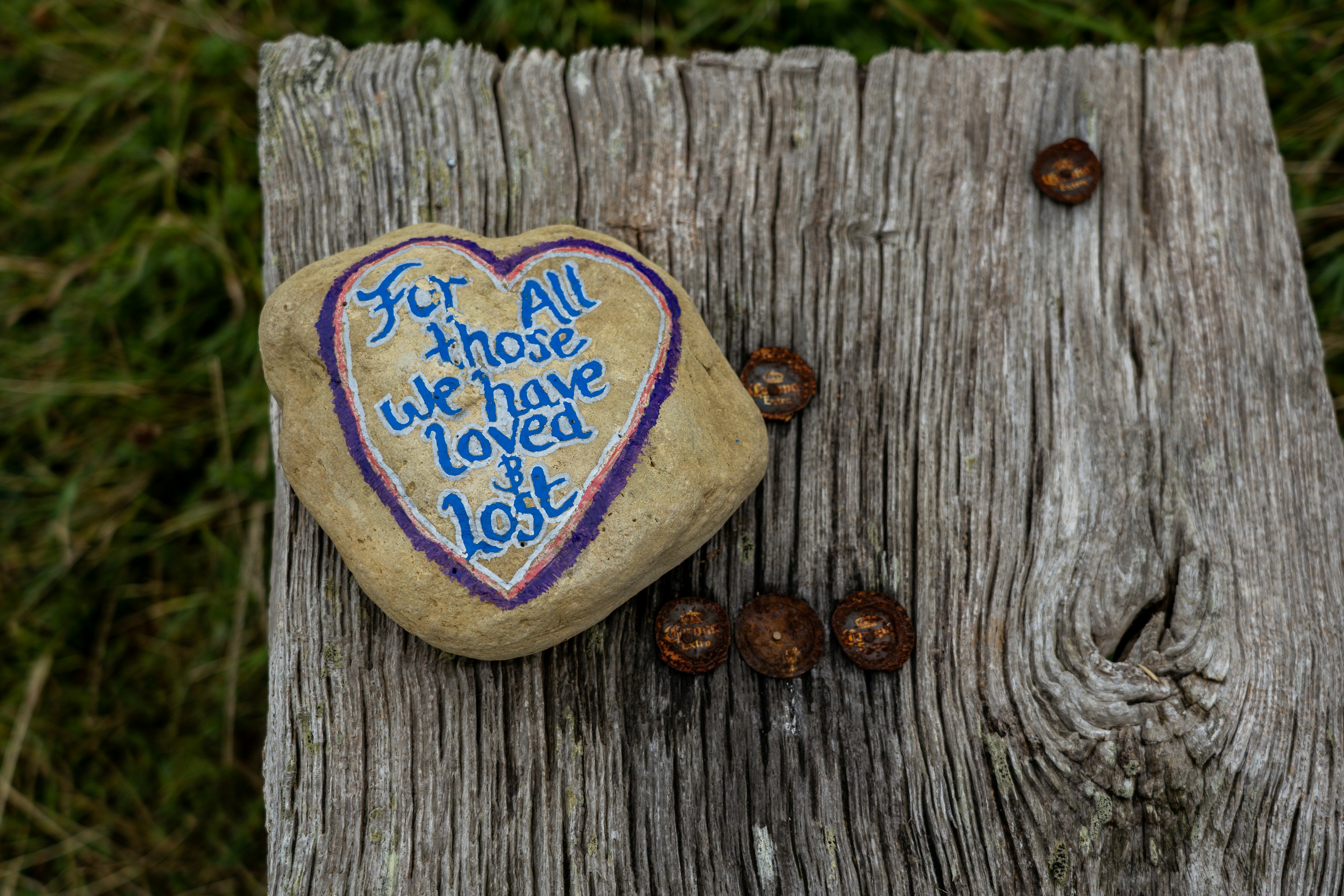 Ein herzförmiger Stein mit der Aufschrift „For all those we have loved & lost“ auf einem verwitterten Holzzaun